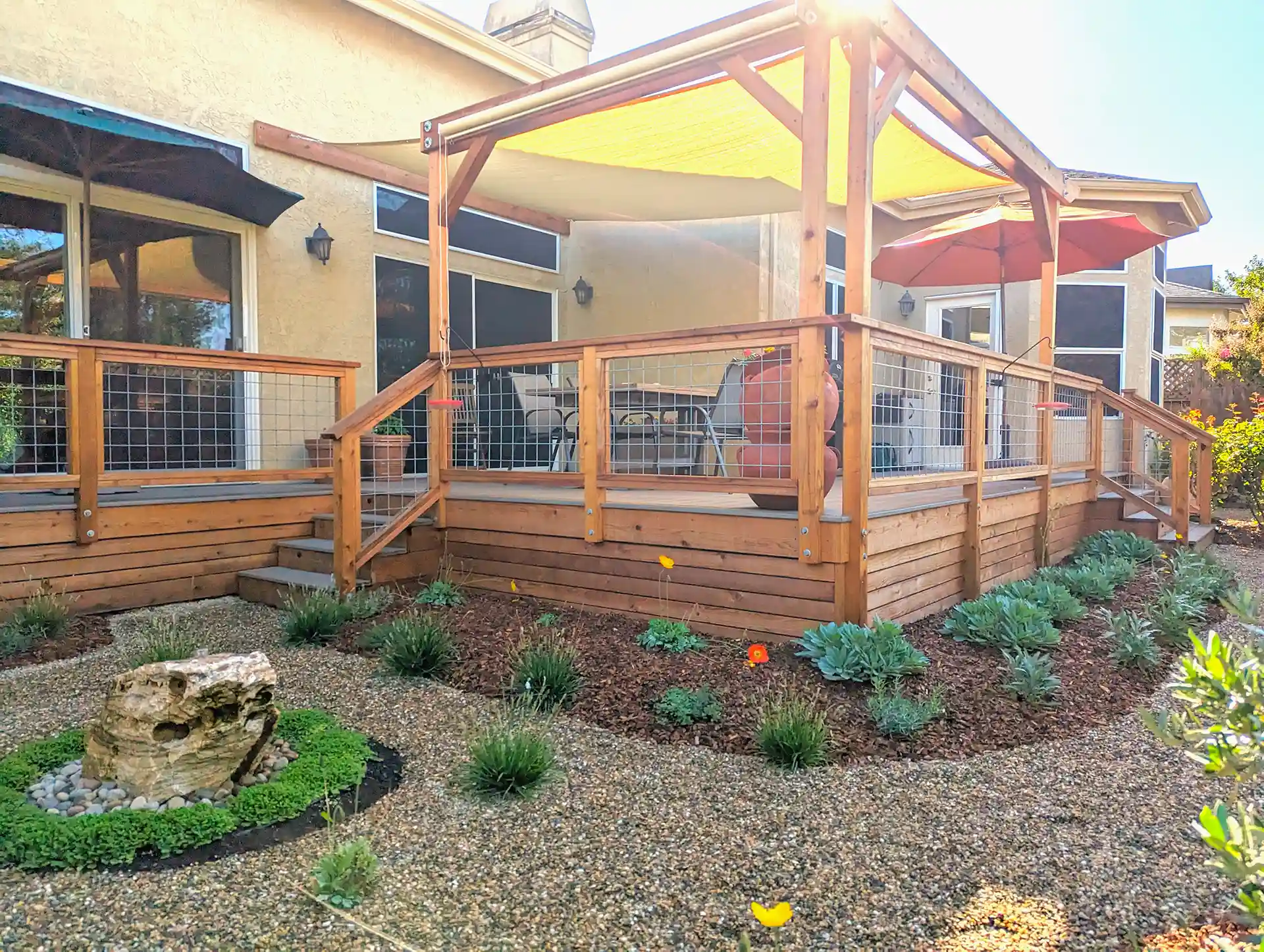 Elevated redwood deck with pergola, cable railing, and tension shade canopy