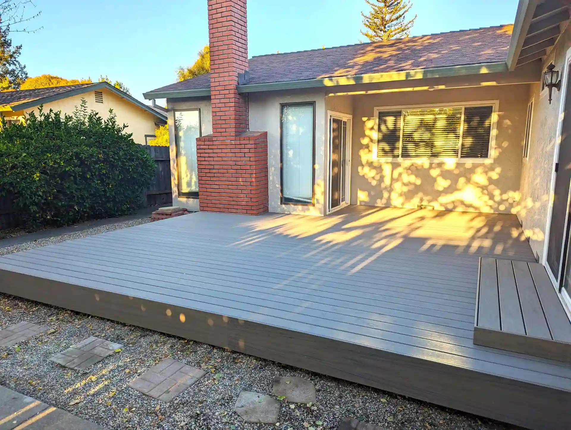 Gray composite deck with integrated bench seating, built flush to patio outside a stucco home with brick chimney
