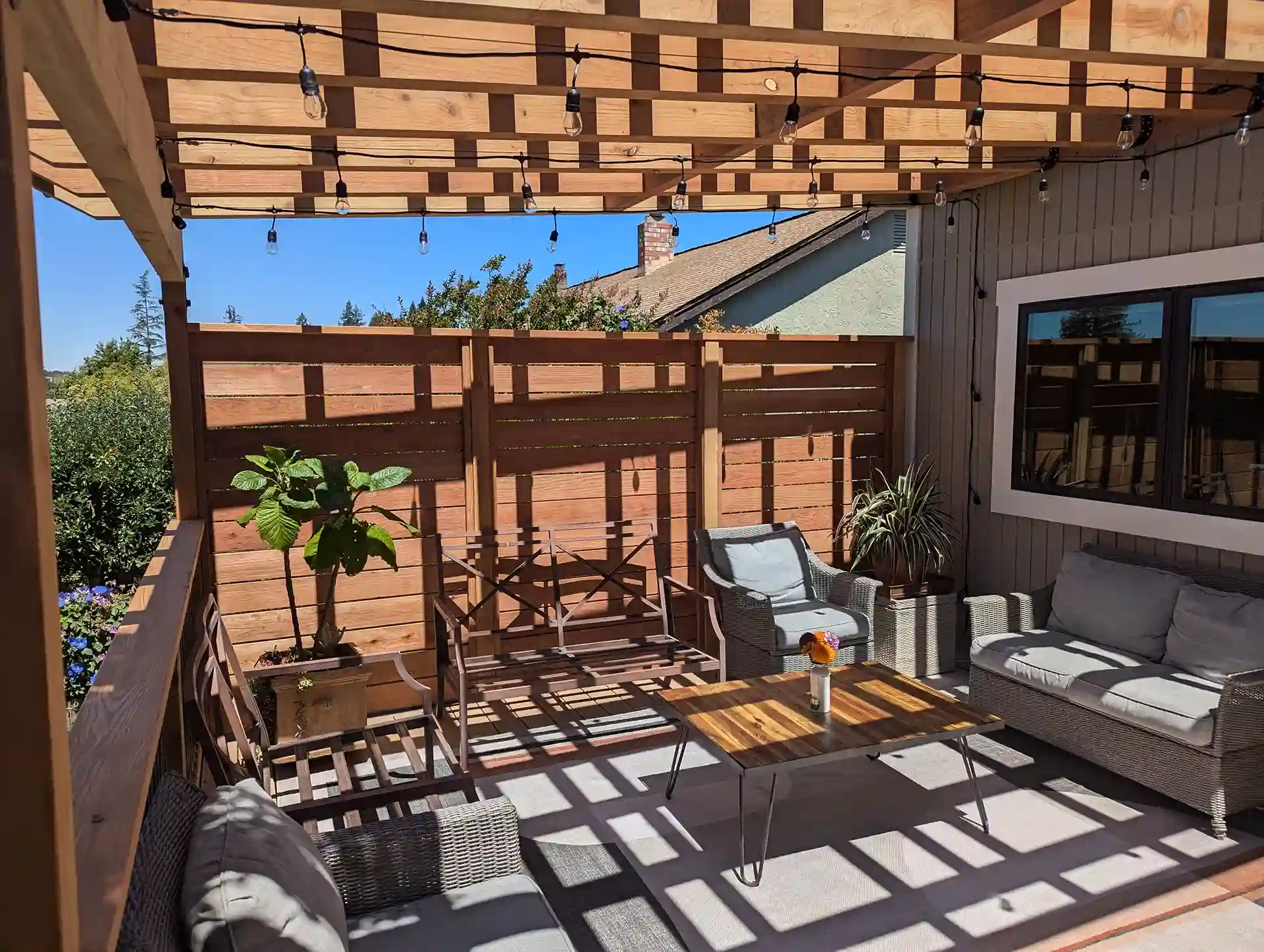 Covered wood deck with privacy wall, outdoor seating, and string lighting for a cozy backyard living space.