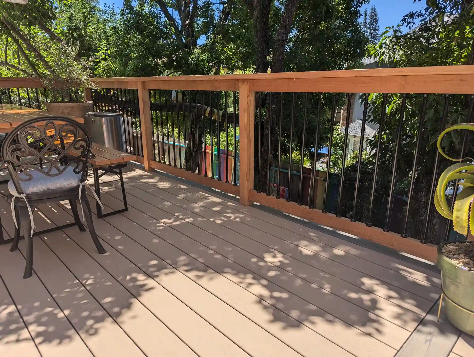 Wood deck with black metal railings and built-in seating area in a shaded backyard.