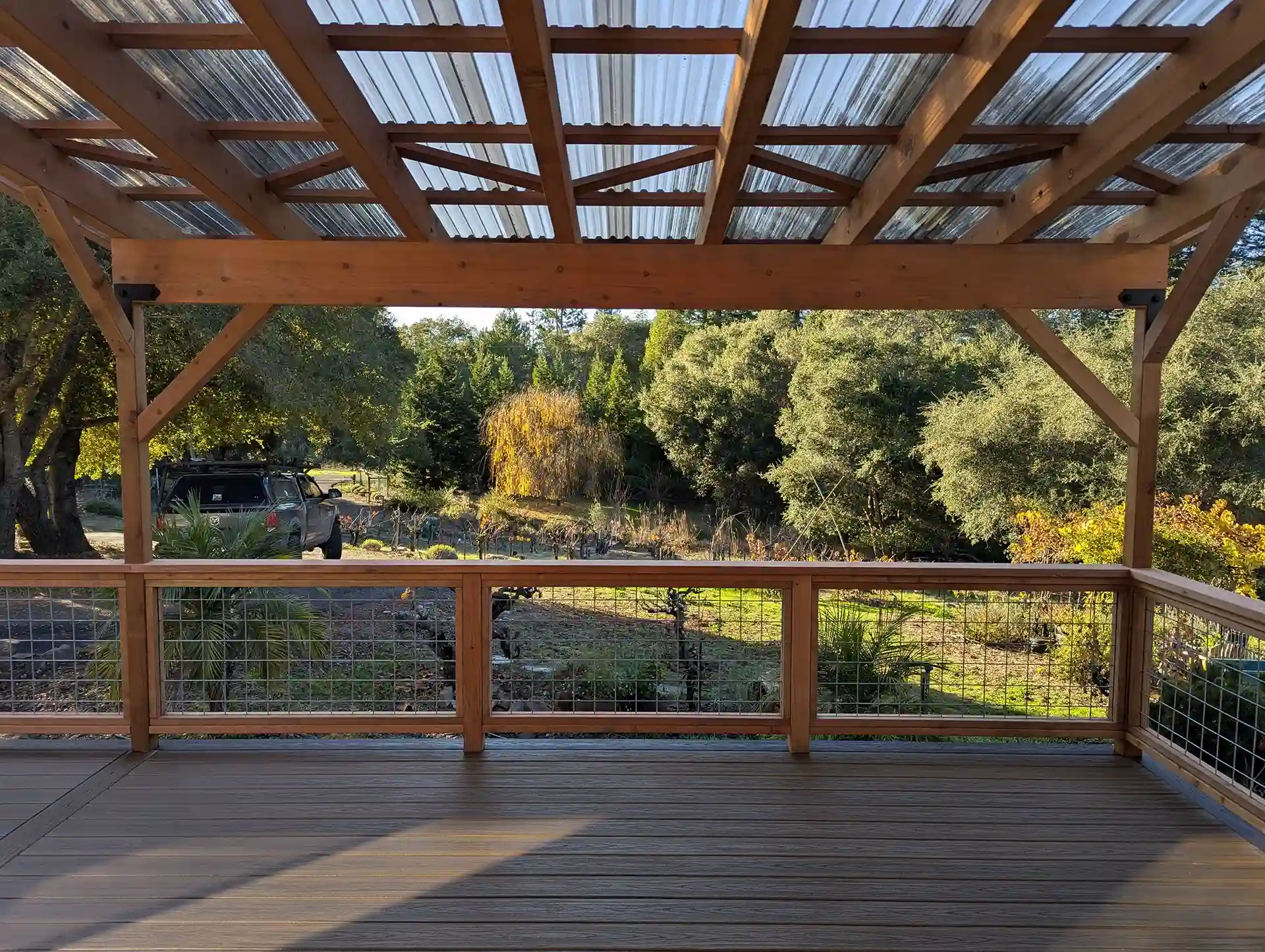 View from a raised composite deck with a clear polycarbonate pergola roof and wire railing