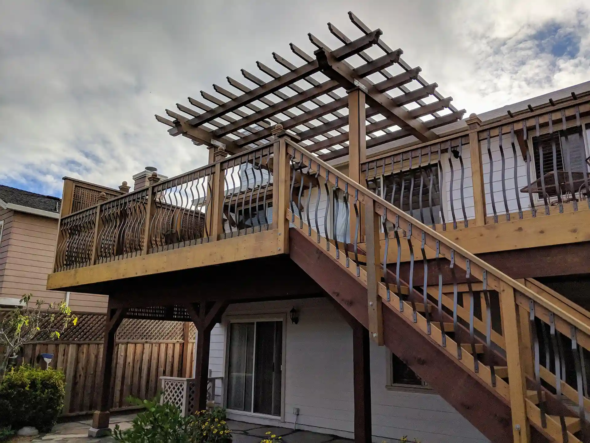 Deck with wooden railing and a pergola above, featuring stairs leading down to the ground level. 