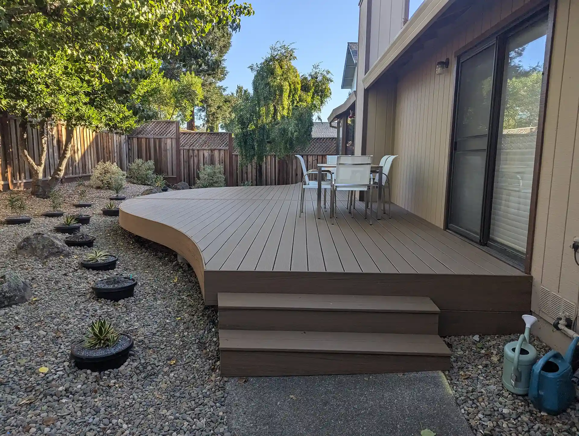 Curved deck with a seating area and stairs, surrounded by landscaping and gravel. 