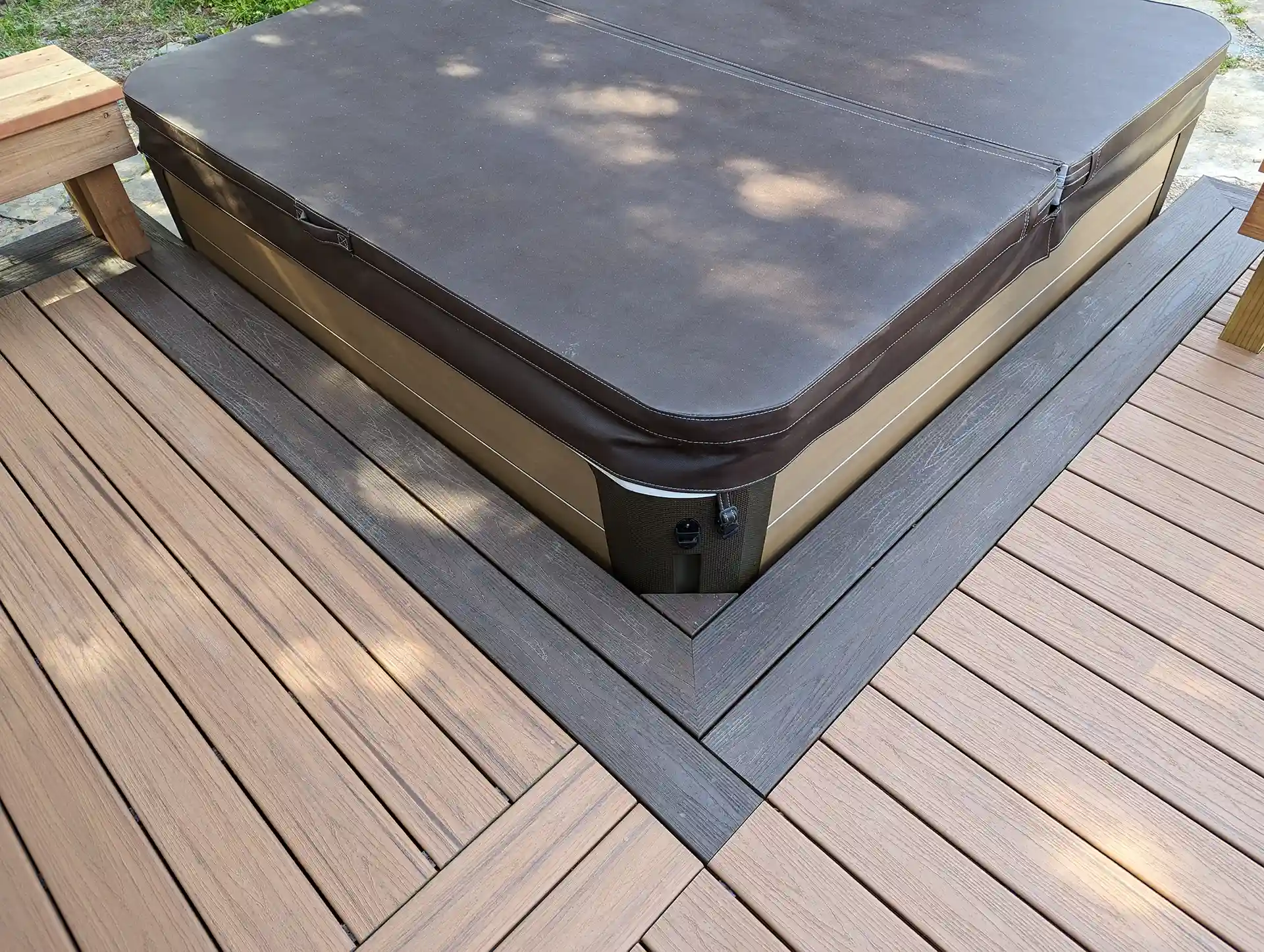 A Trex Transcend composite deck with an inset covered spa, bordered by dark lava rocks and a black metal tiki torch.
