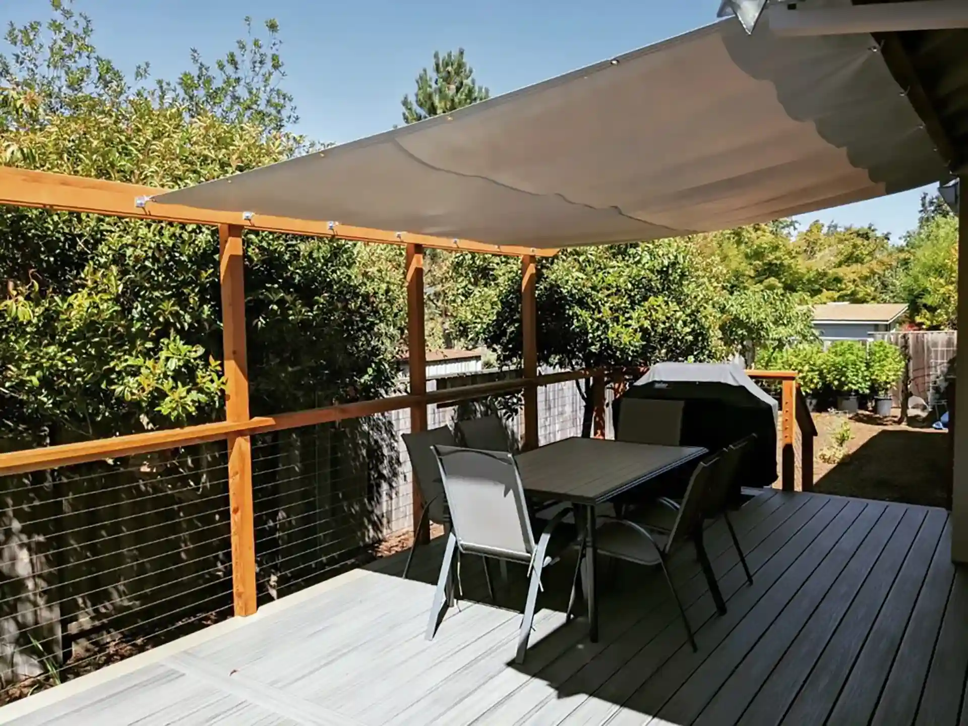 Single-level Trex Transcend Island Mist composite deck with cable railing, outdoor dining furniture, grill, and overhead fabric shade canopy in a private backyard. 