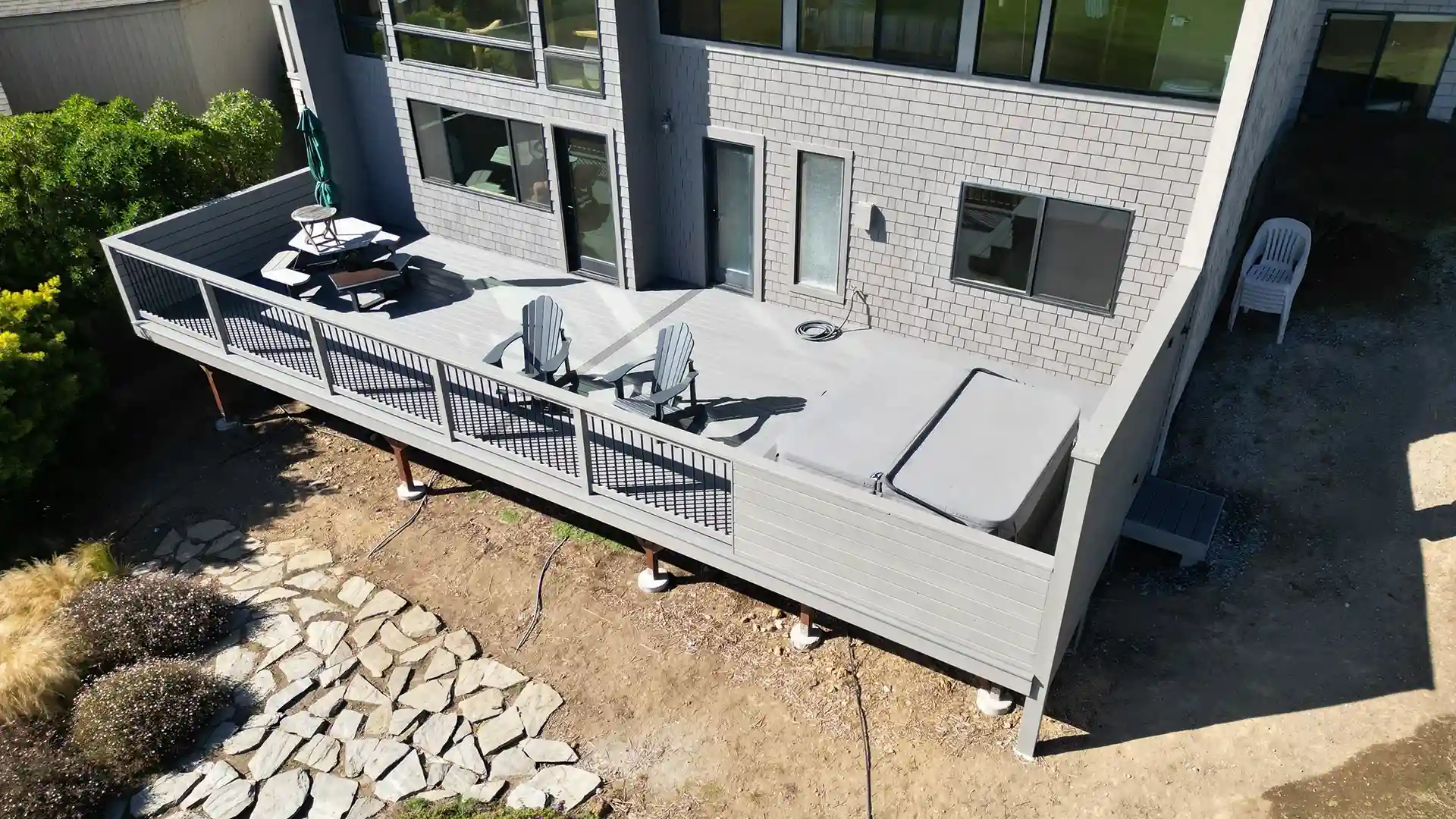 Modern composite deck with gray boards, a hot tub, and a seating area, featuring a clean, minimalist design and large windows in the background.
